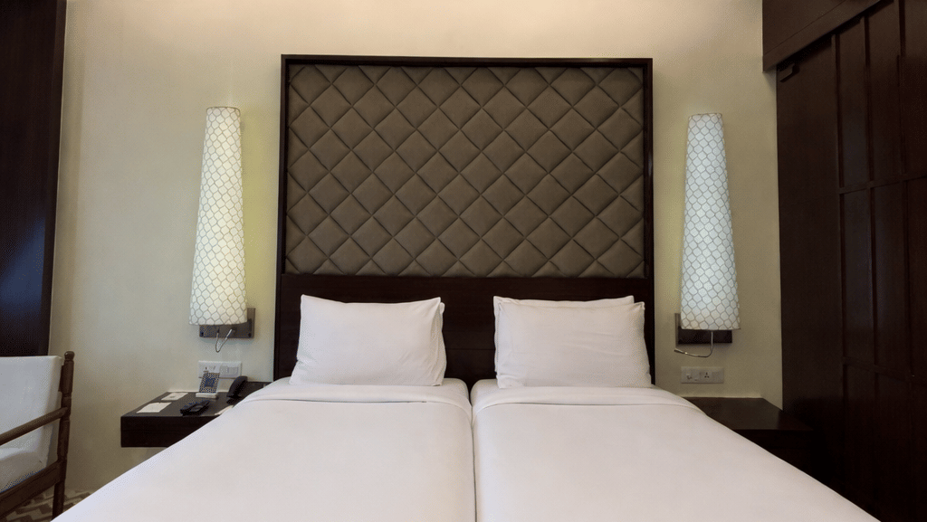 Twin beds with tall, patterned headboards and white linens beneath a ceiling fan in the Superior Twin room at Clarks Amer, Jaipur.
