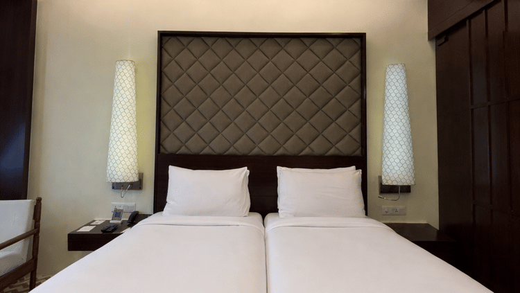 Twin beds with tall, patterned headboards and white linens beneath a ceiling fan in the Superior Twin room at Clarks Amer, Jaipur.