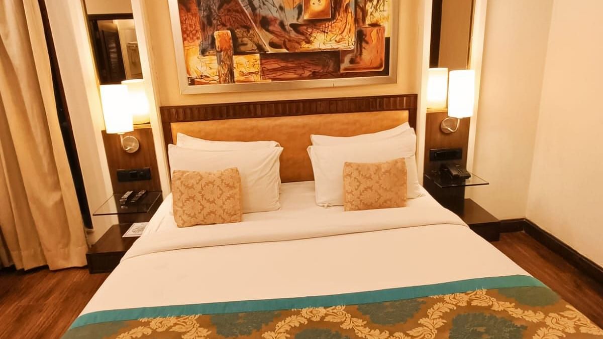 Suite with a double bed neatly arranged with plush pillows, bedside tables each topped with a lamp, and a photo frame on the headboard at Inde Signature Tower, Gurgaon