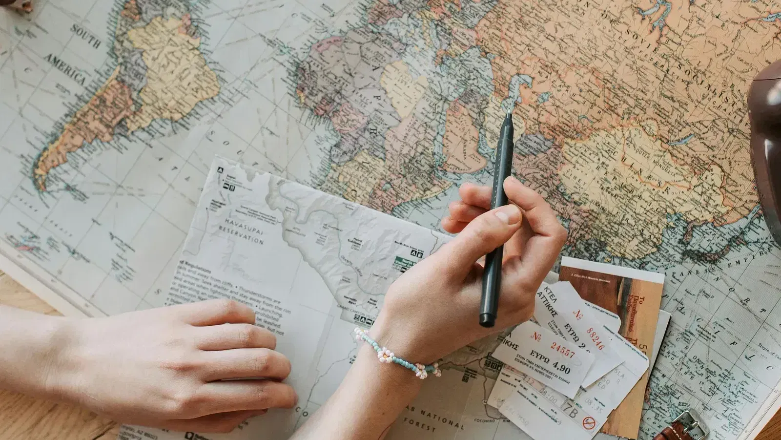 A person's hand holding a pen and hovering over a world map.