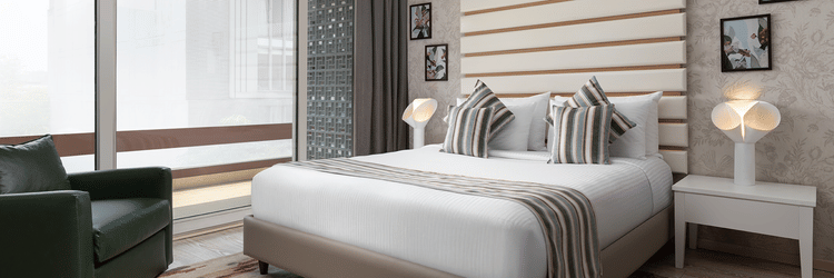 A stylish room at The Atara, Gurugram boasts a comfortable bed with a patterned runner, a plush green armchair, and a large window that offers a scenic outdoor view