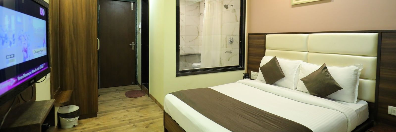 A bedroom at Krushnai Resort with a large TV, a king size bed, and a partial view of the bathroom through a glass wall.