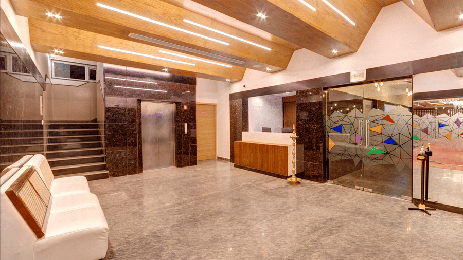 A white sofa, grey marble floor, wooden ceiling, and stairs in the lobby of Icon Express By Bhagini, Mahadevapura.