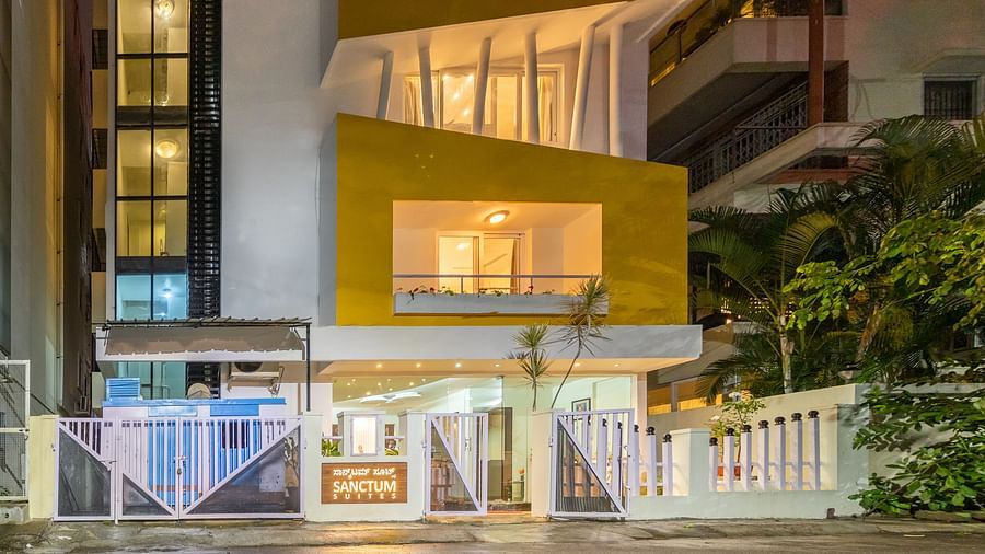 A facade of Sanctum Suites Domlur, Bangalore with warm lighting and view of balconies shot at night.