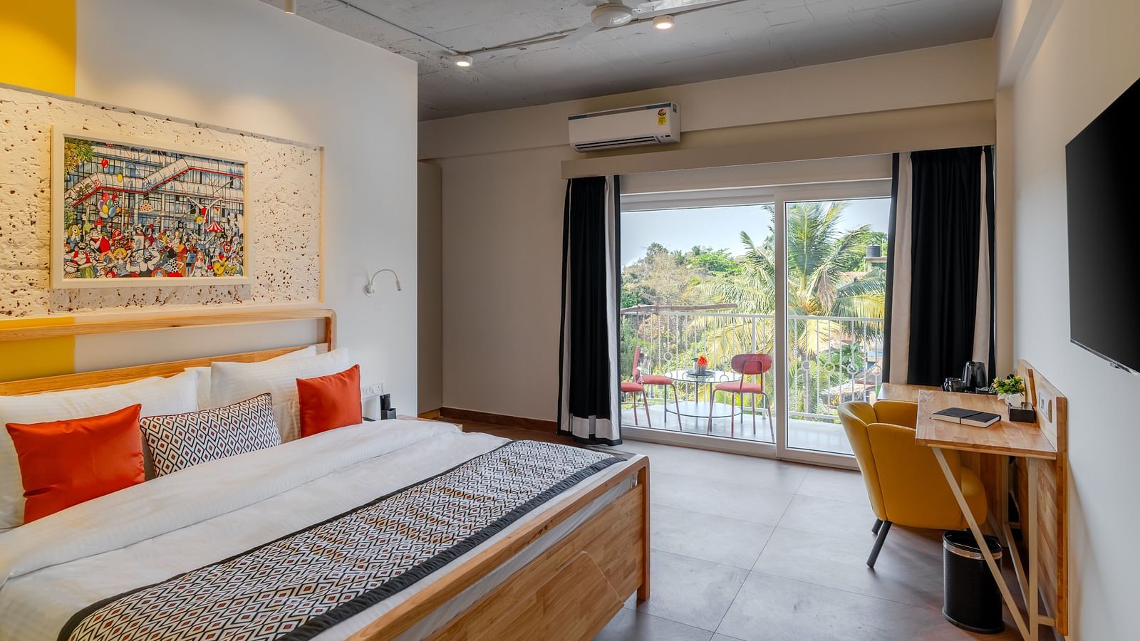 Bright hotel room with, flat TV screen, work desk and chair, vibrant art on the wall, and an access to the balcony at Bedzzz Xclusiv Morjim, Goa