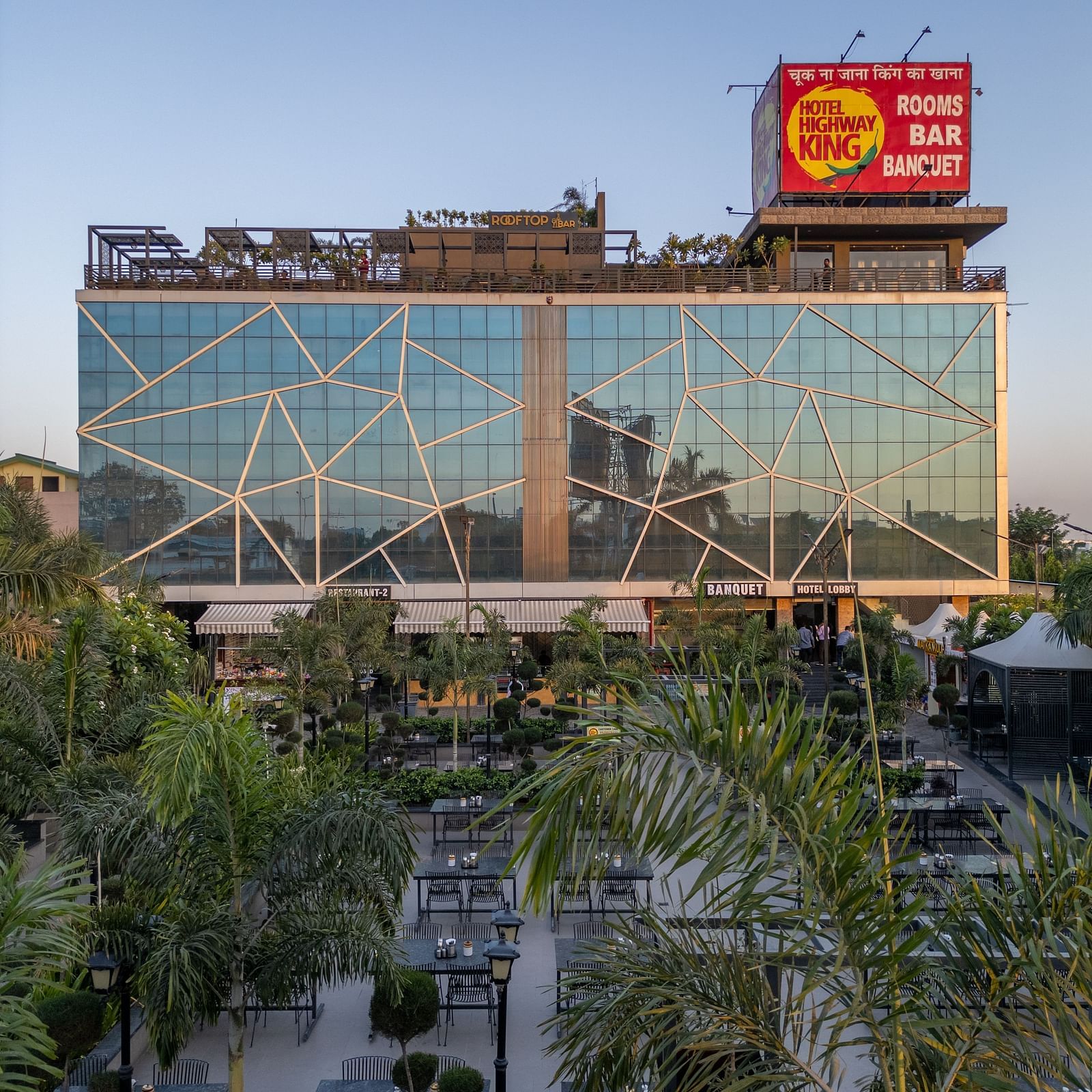 Exterior view of Hotel Highway King with glass facade and signage, surrounded by green trees.
