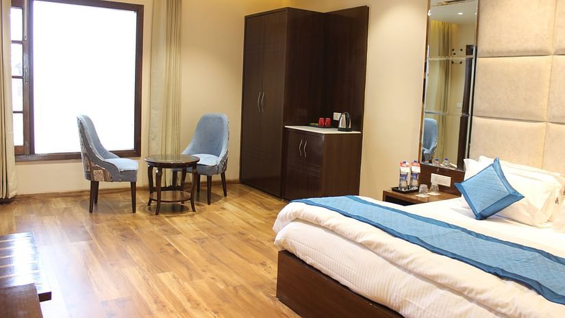 Side angle view of the Superior room with plush bed with bedside tables scenic view from the window with curtains and seating area - Mastiff  Hotel, Dalhousie