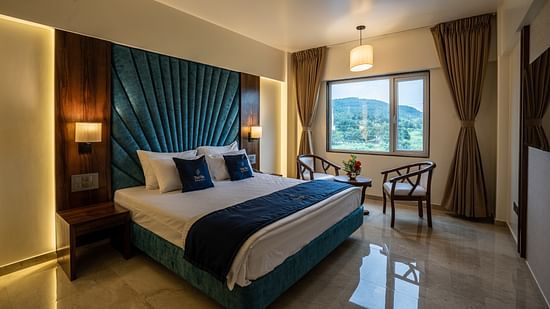 View of Suite with king sized bed and bedside tables seating area with windows and curtains - Mastiff Grand - The Sia Palace Suites Banquets Khopoli
