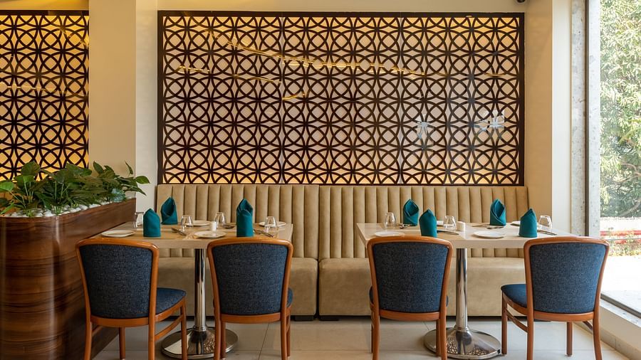 Dining area at Mastiff Grand The Sia Palace Suites & Banquets, Khopoli, with tables set, a banquette, and a large decorative jali screen on the wall.