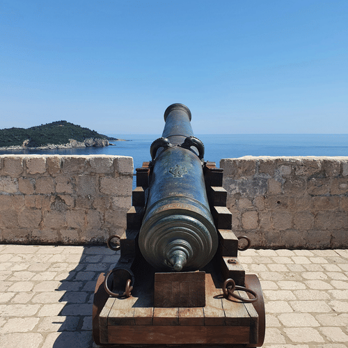 Historic cannon overlooking a water body from a fort under clear skies.