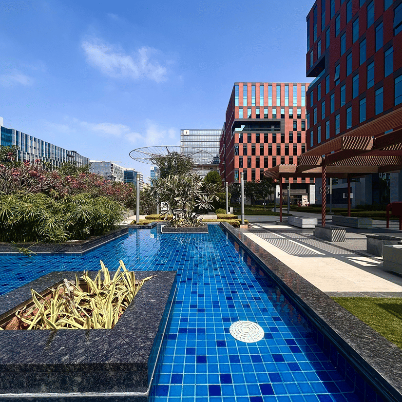 A modern outdoor pool area features blue tiled water alongside stylish, contemporary brick-coloured commercial buildings.