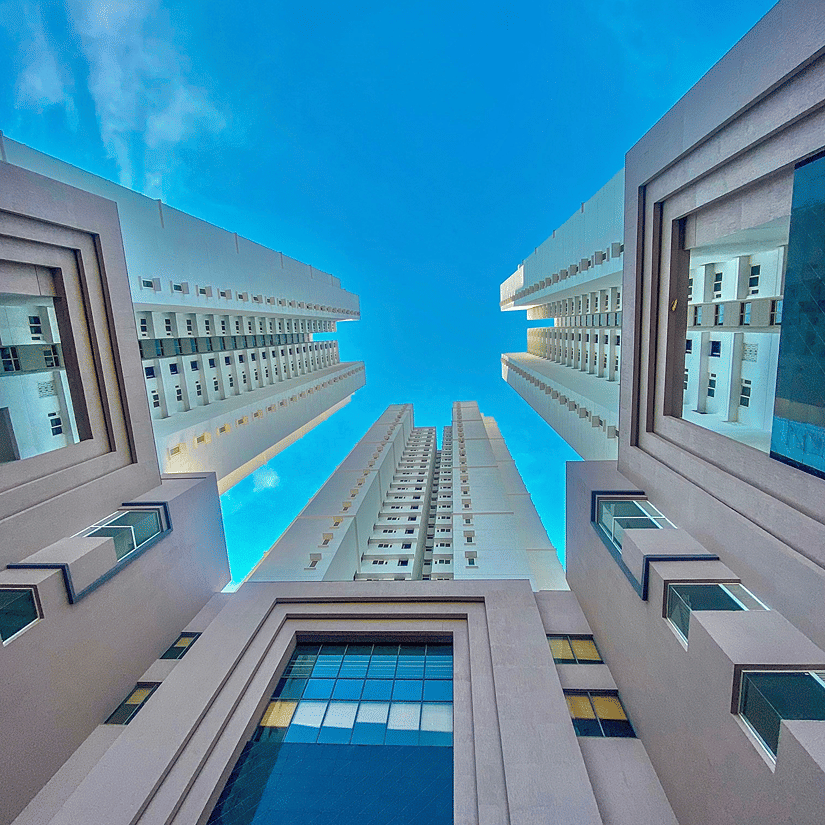 A low-angle perspective looks directly up at towering white and glass modern skyscrapers reaching into a clear blue sky.