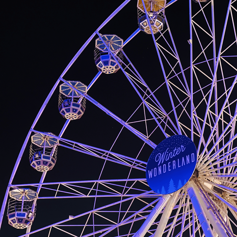 A view from below of a ferris wheel with the signage Winter Wonderland (Doha), seen during night time.