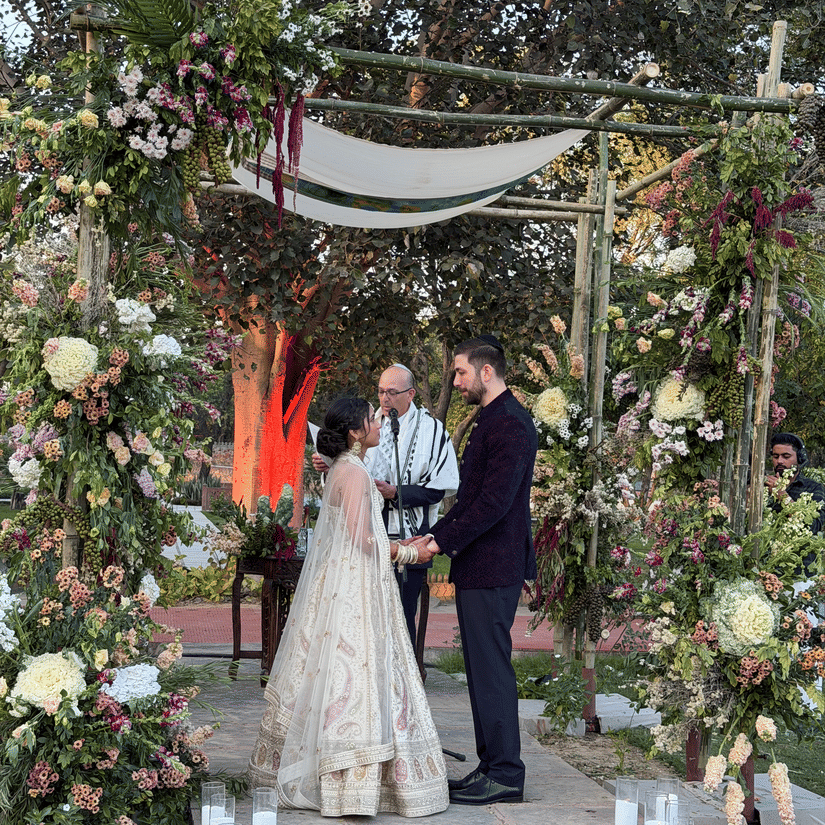 A bride and groom standing before a beautifully decorated outdoor floral altar with candles lining the aisle at Umaid Palace.