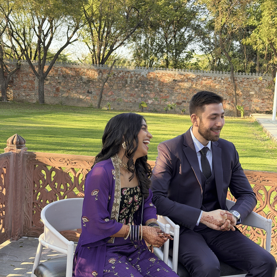 A couple dressed in elegant formal attire sits together on a stone terrace overlooking a green lawn at Umaid Palace.