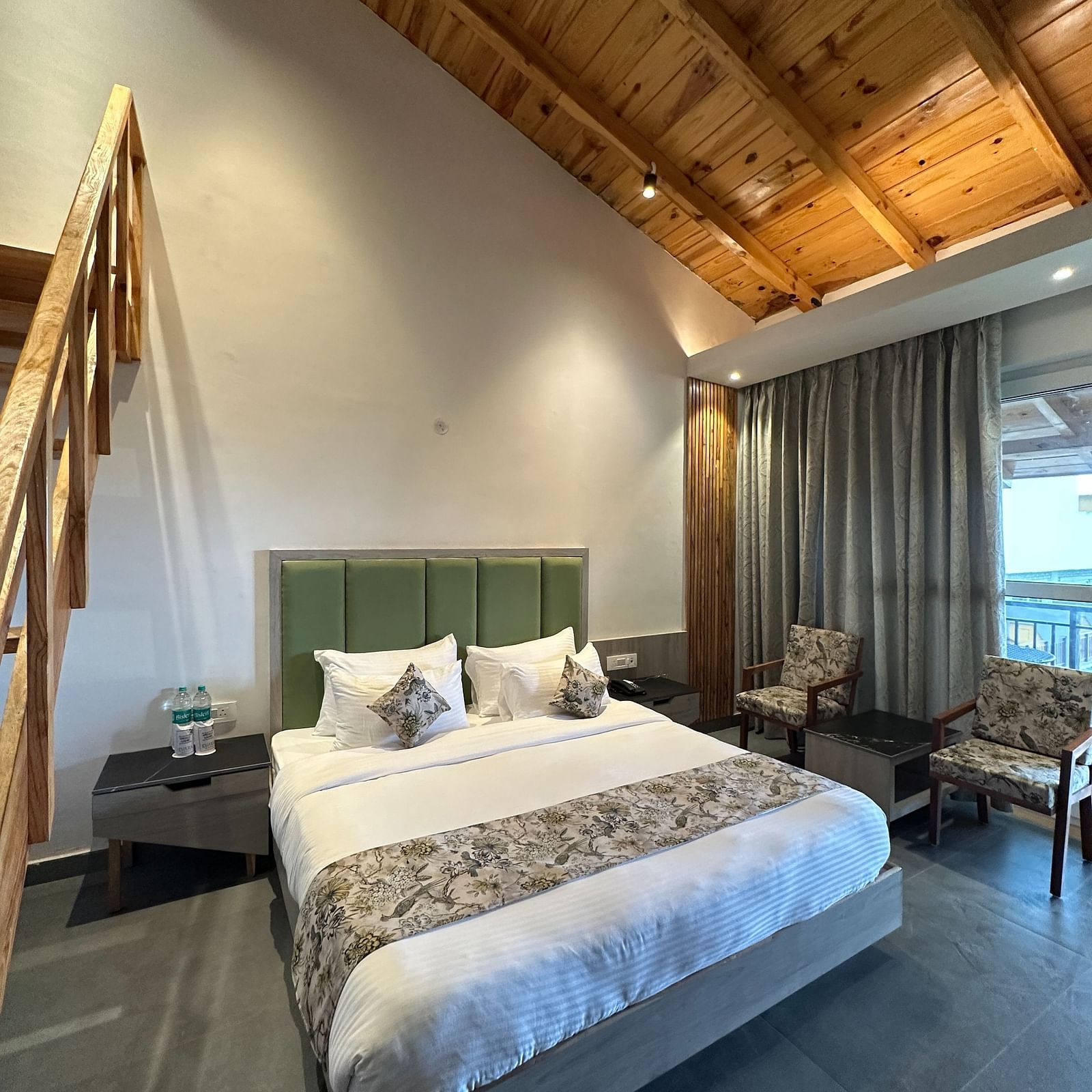 A spacious hotel room with a king size bed, a wooden ceiling, and a large window overlooking a scenic view.