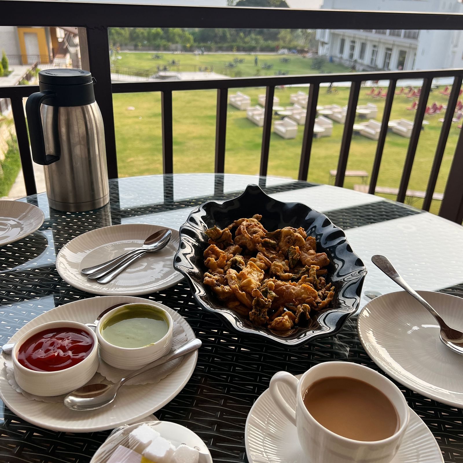 A breakfast spread on a balcony overlooking a golf course, featuring a cup of tea, a plate of crispy fries with dipping sauces, and a water bottle.