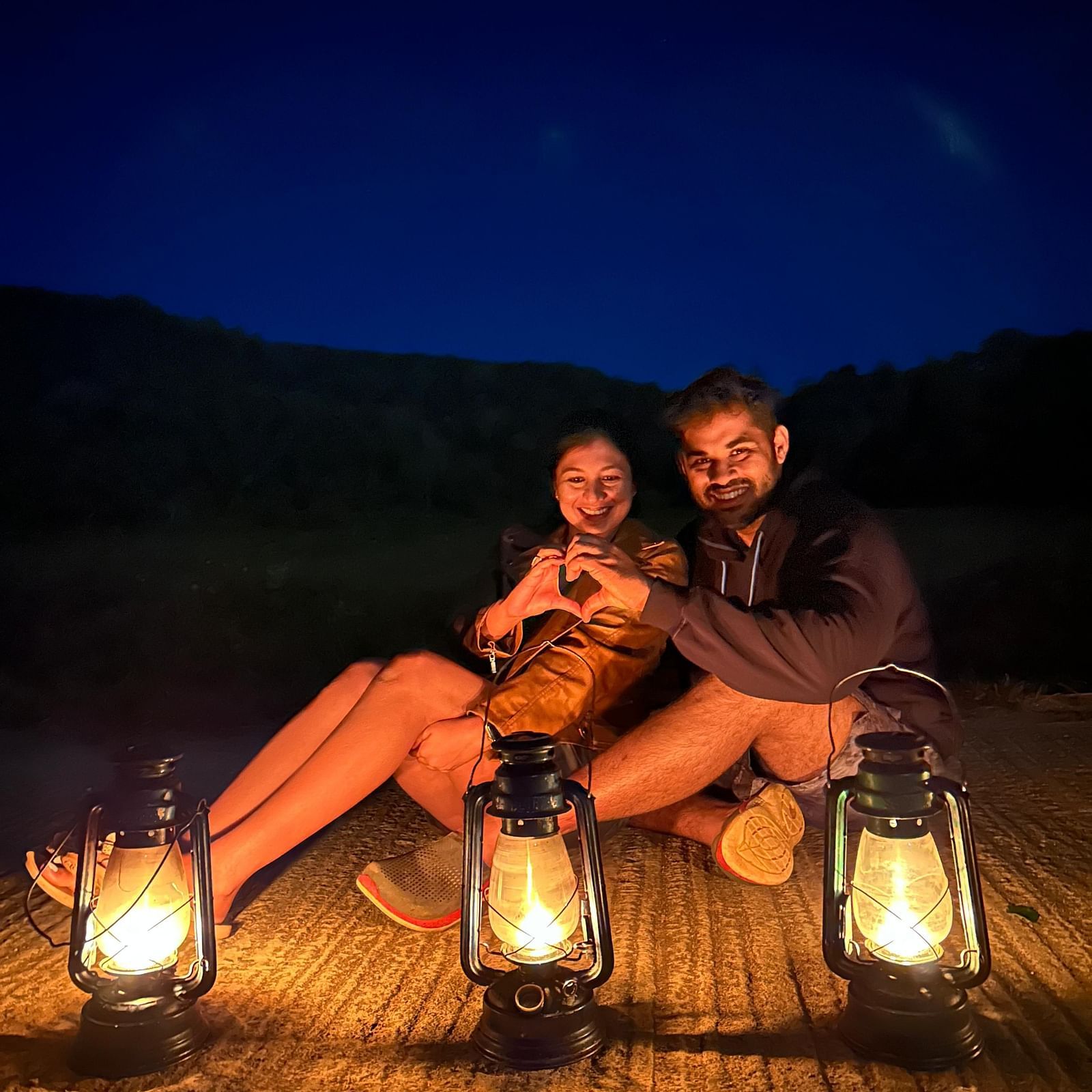 A couple posing for the camera with three lanterns in front of them and a dark blue sky in the background - Evergreen County