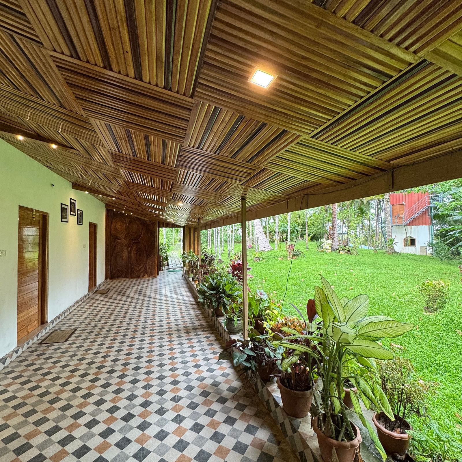 A long covered patio or hallway with a patterned tile floor, potted plants, and an intricately designed wooden ceiling.