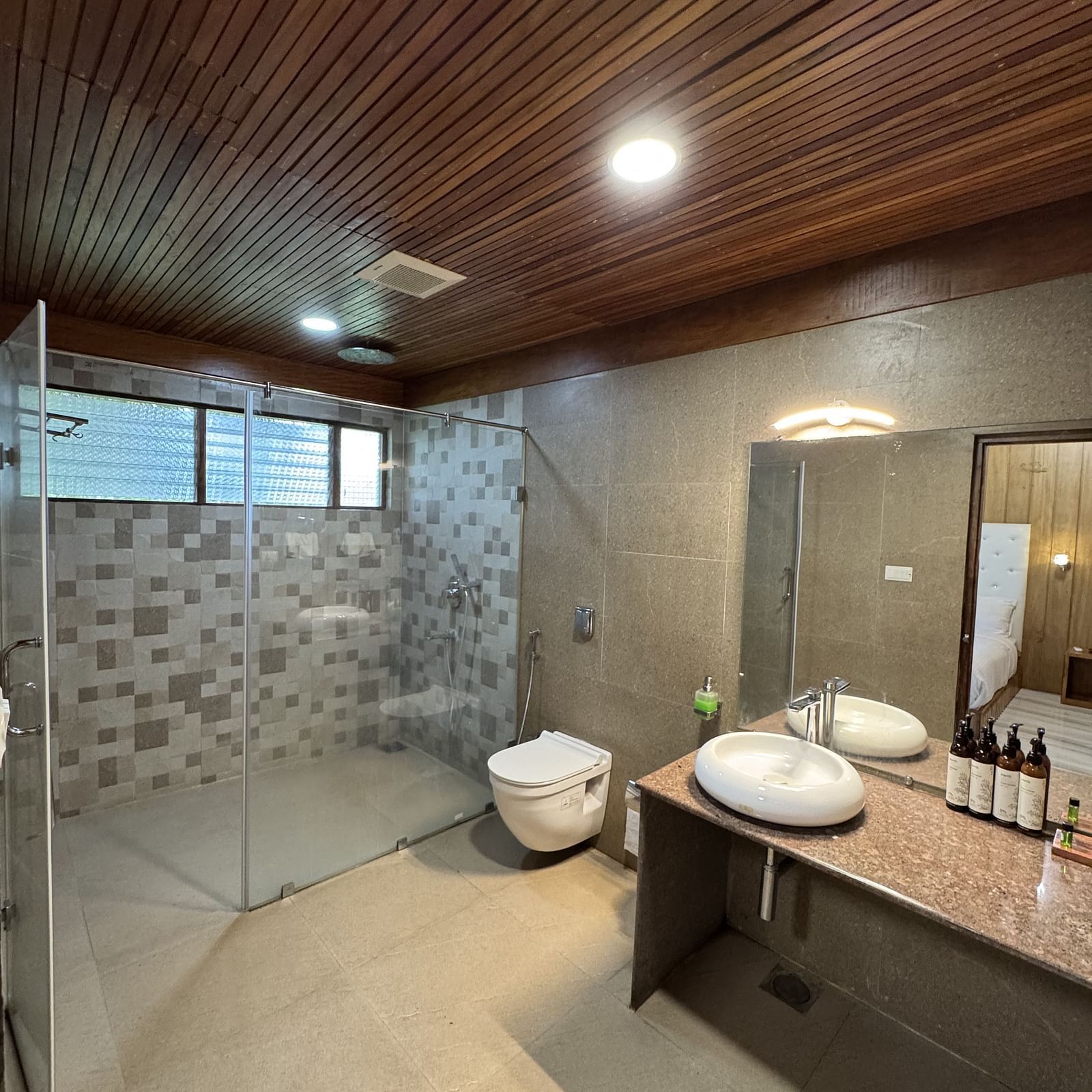 A spacious bathroom with two stone-like sinks on a wooden vanity, a large mirror, and textured wall tiles.