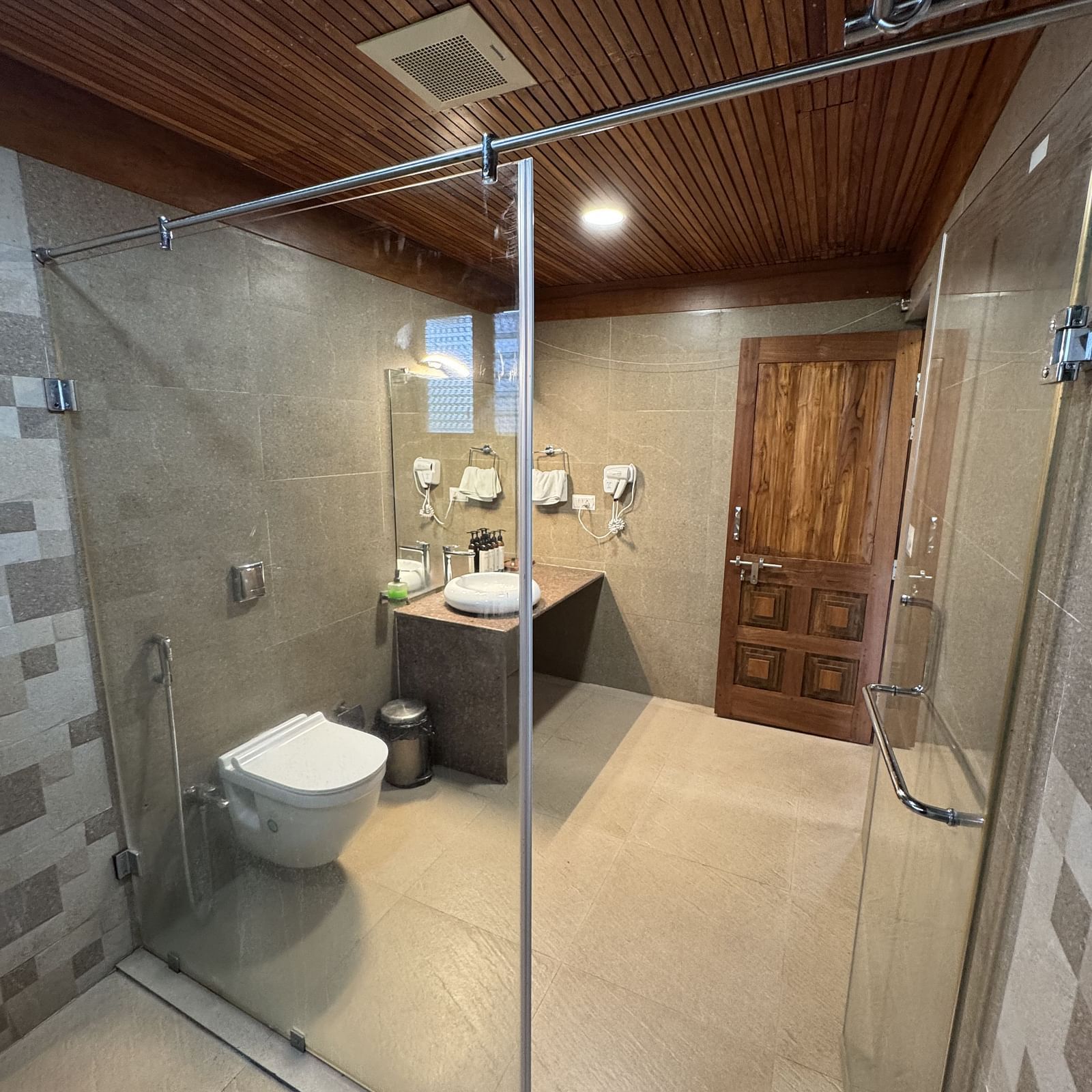 A spacious bathroom with two stone-like sinks on a wooden vanity, a large mirror, and textured wall tiles.