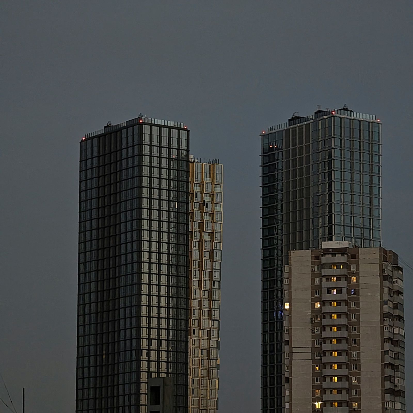 Dimly lit photo of two urban buildings at dusk, one with warm interior lights.