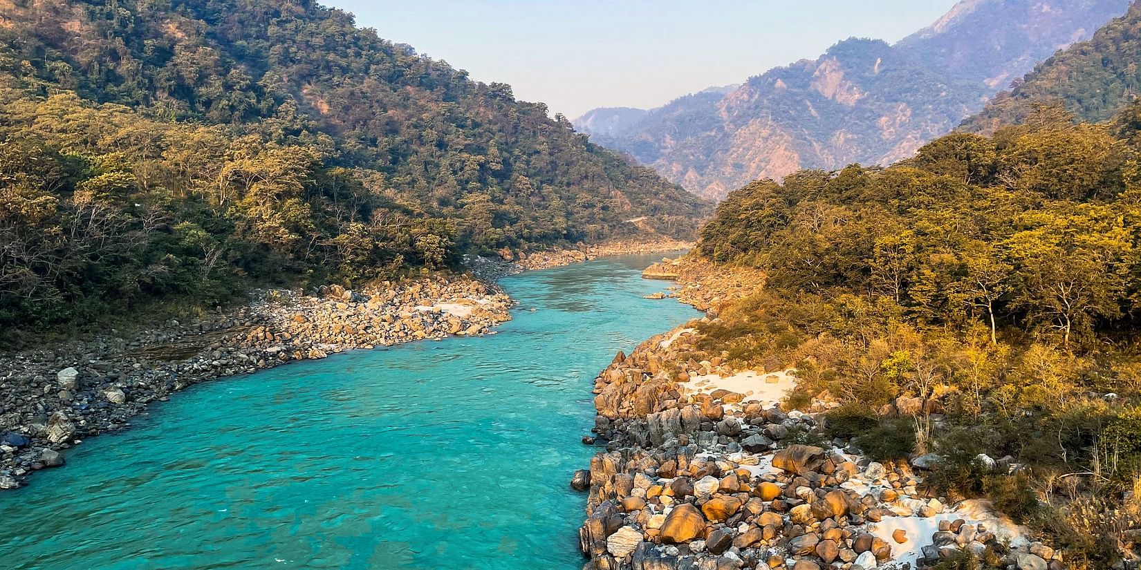 The holy river Ganga flowing in between the hills with clear sky in the background.