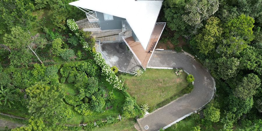 A light-colored modern villa surrounded by tall trees and tropical vegetation in daylight at Ibex Resorts, Coonoor (Tapas).