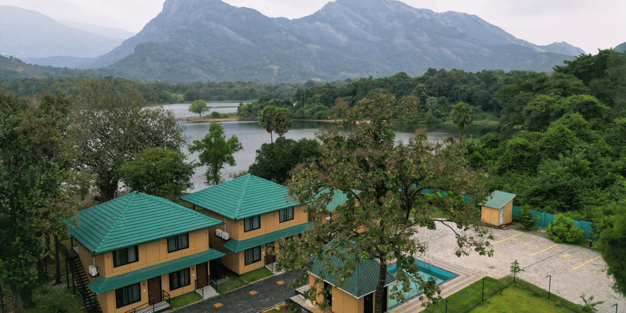 High-angle landscape view of the resort buildings situated between a calm lake and towering mountain peaks - Ibex Resorts, Malampuzha (Kava Eco Camp and Caravan Park)