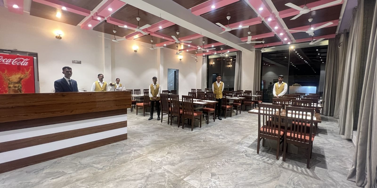 Wide view of the fine-dining restaurant at Daksh The Valley Resort, Saputara, showcasing its vibrant ceiling, neatly arranged dining tables and the staff standing there.