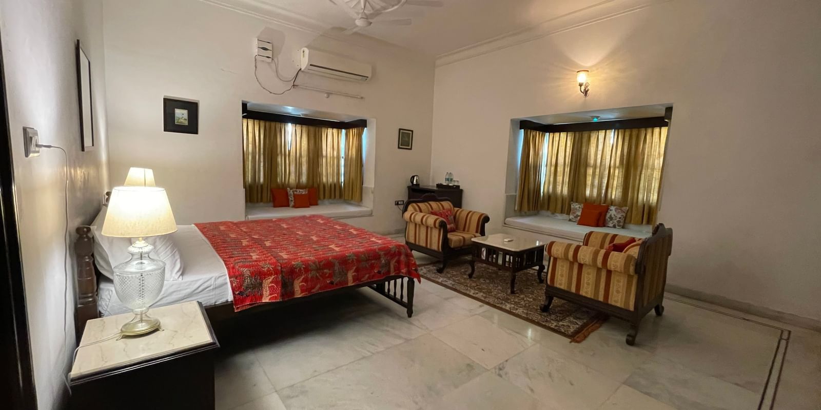 A panoramic view of the Heritage Courtyard Room at Mahendra Niwas, showcasing a spacious seating area with a sofa, an armchair, and a coffee table.