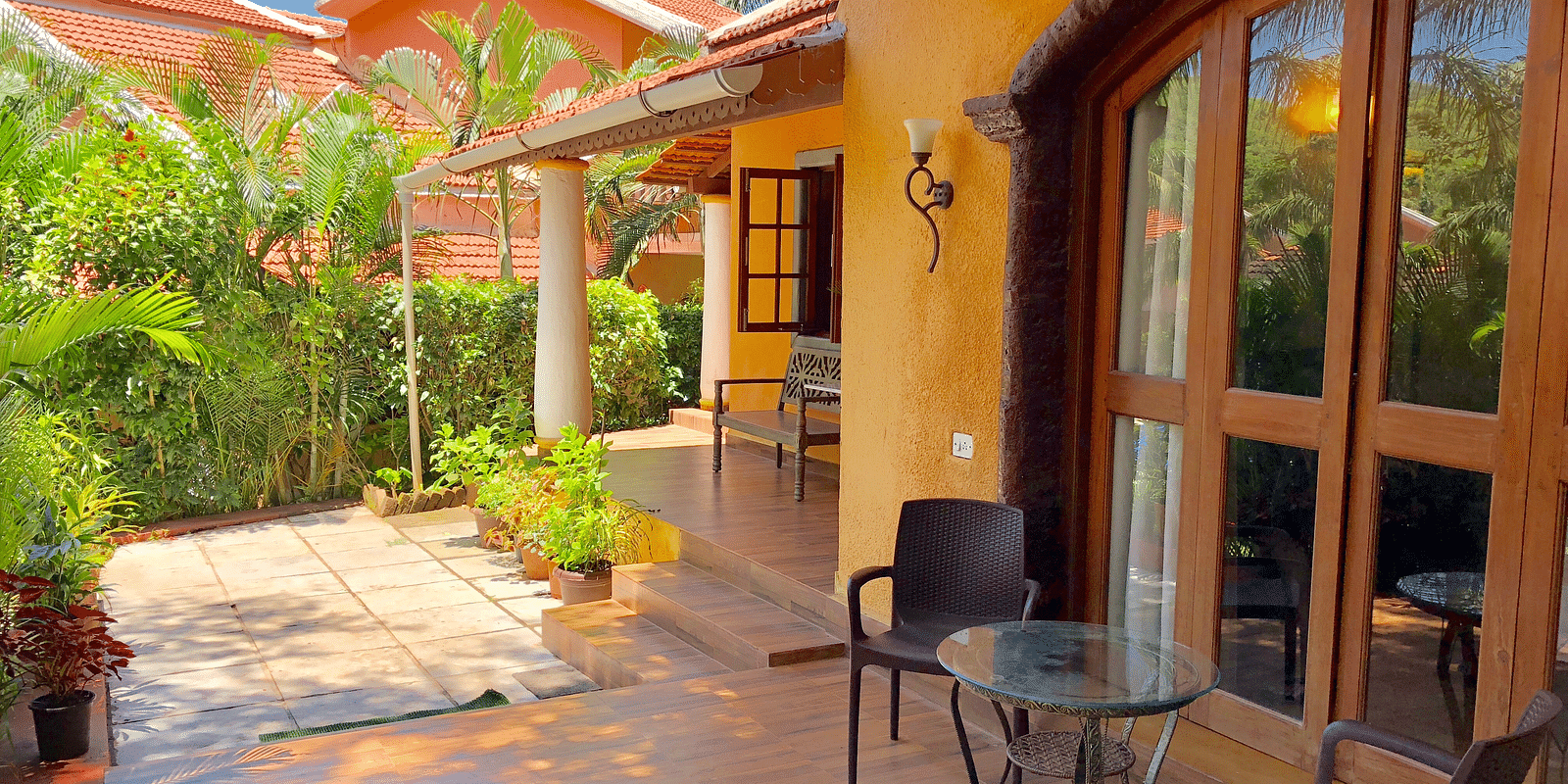Exterior sitting area during daytime at The Bungalows Light House, Goa featuring a coffee table and a pair of chairs with lush greenery in the surroundings