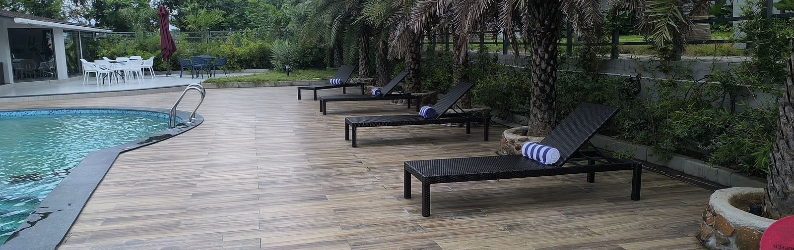 Poolside view with deck chairs and palm trees on a wooden platform at Trishvam Symphony, Krishnagiri.