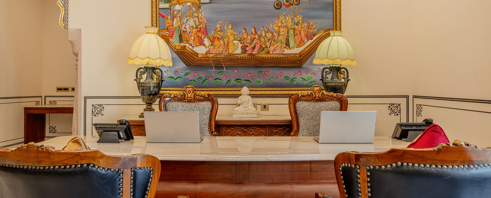 the reception area with the table and two laptops kept over it along with a beautiful painting behind it - Brij Castle, Jaipur