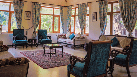 A lobby lounge area featuring armchairs, a sofa, a central rug, and multiple curtained windows at Amantra Shilpi Resort, Udaipur.