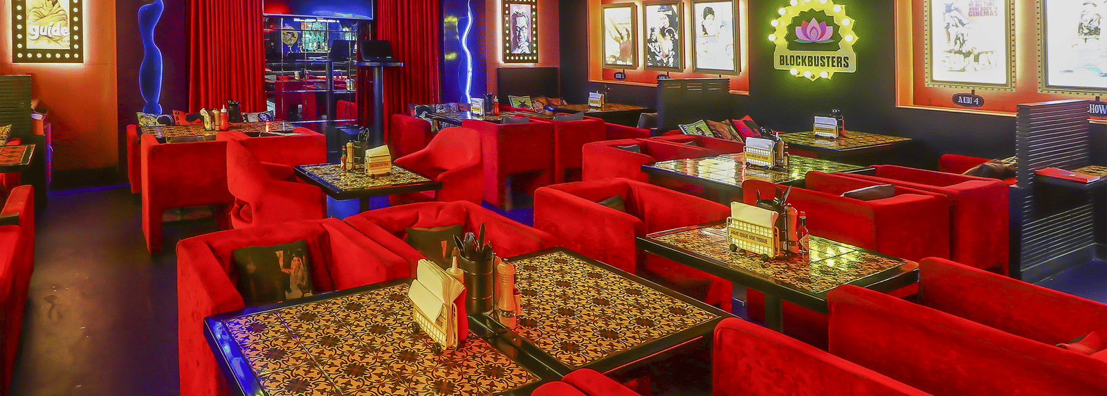 A restaurant hall with multiple red sofas, framed posters and bright neon lights at Infiniti Hotel, Indore.