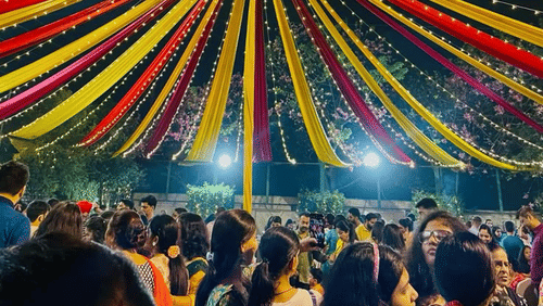 Crowd dancing under colourful canopy lights at a lively Dandiya celebration.