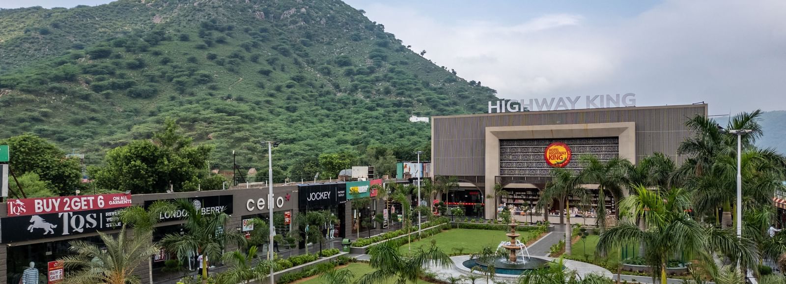 Diagonal exterior view of Hotel Highway King, Neelka, set against a cloudy sky with lush mountains in the background.
