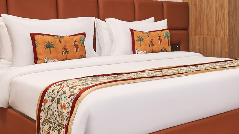 Bedroom at Triptam Hotel, Vrindavan featuring a plush bed with bed runner and pillows against a patterned wall on wooden floor