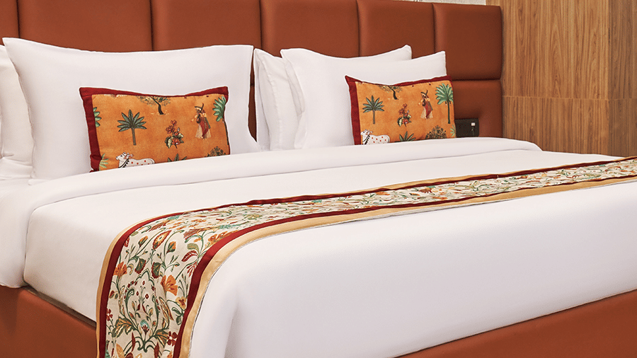 Bedroom at Triptam Hotel, Vrindavan featuring a plush bed with bed runner and pillows against a patterned wall on wooden floor