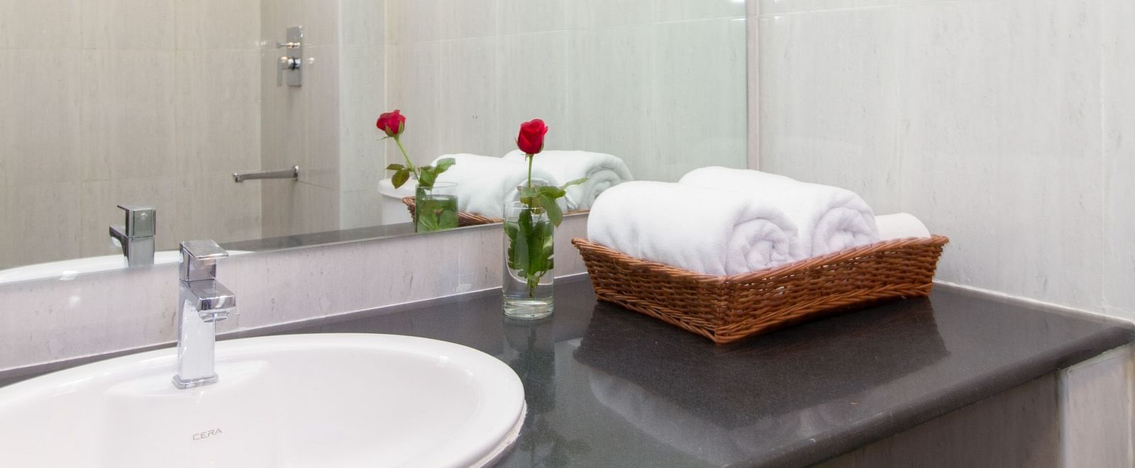A bathroom with a sink with a vase of red flower and neatly folded white towels at Sanctum Suites Whitefield, Bangalore.