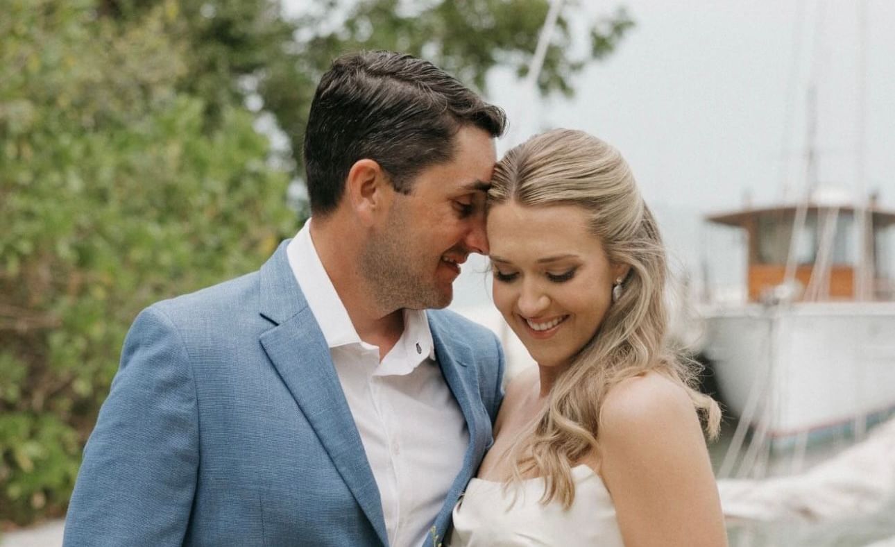 A portrait-shot of a couple with the woman holding a bright flower bouquet, standing on the waterfront property of Casa Morada.