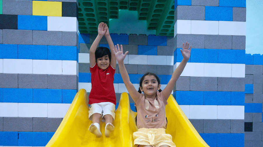 2 happy children slide down a double slide next to a toy brick castle wall at Tic Tac Tot.