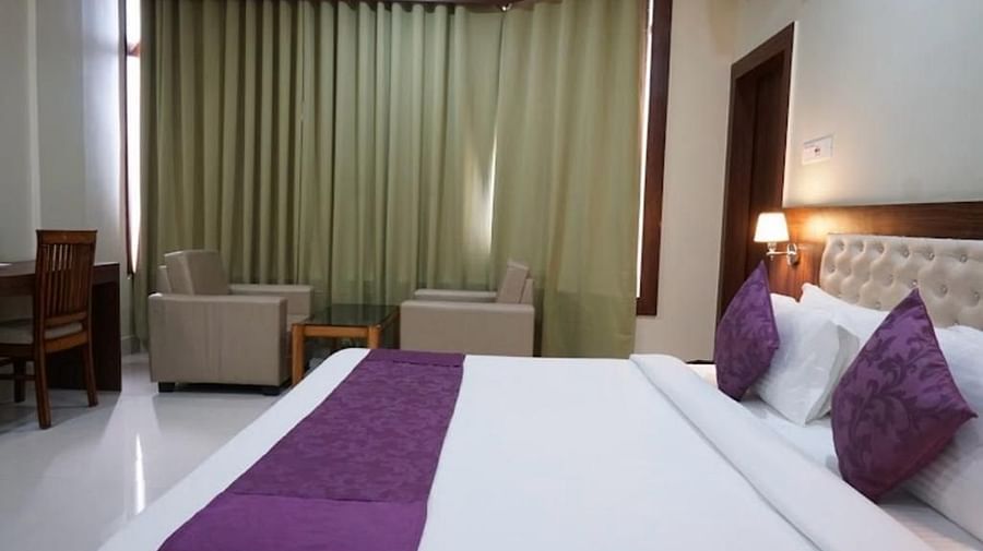 A well-lit room with plush seating, purple bedding, and floor-length curtains creating a calm atmosphere - Pemaling Lords Eco Inn Guwahati
