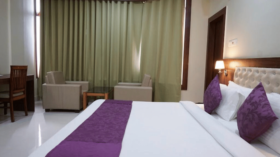 A well-lit room with plush seating, purple bedding, and floor-length curtains creating a calm atmosphere - Pemaling Lords Eco Inn Guwahati.