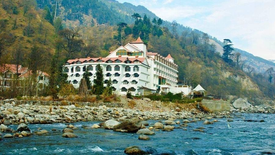 facade of Mastiff Grand, Manali with a river flowing in front of it and surrounded by mountains