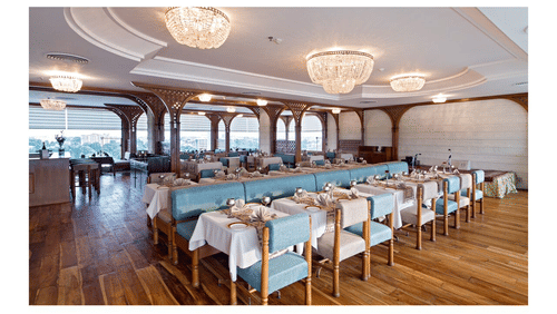 A bright, elegant dining room on a cruise ship or a luxury hotel, with tables set and large windows overlooking the sea or landscape - Clarks Avadh, Lucknow