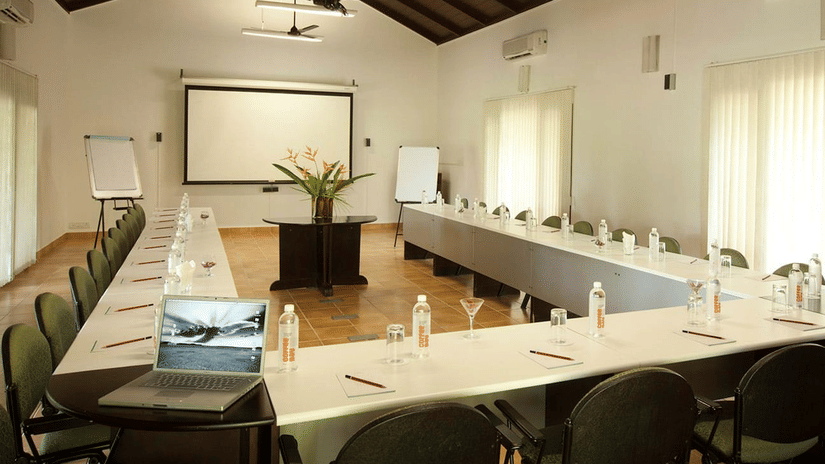 Conference Hall in Bandipur at The serai Bandipur with a U-shaped table and a projector screen under warm lighting