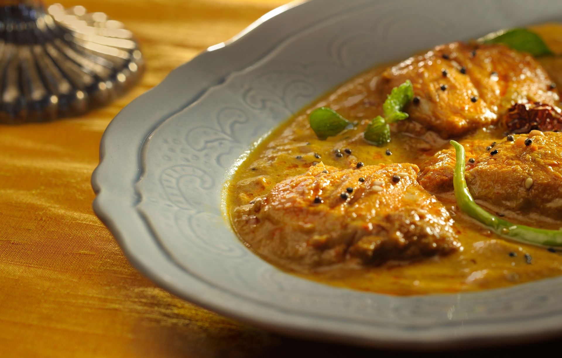 Creamy fish curry with spices and chili garnish.