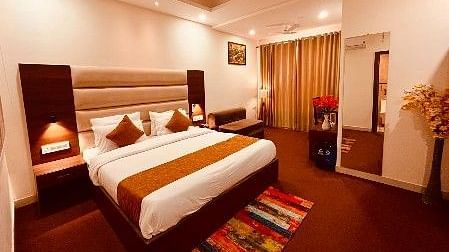 A spacious room with a bed, bed side tables, lamps, and a full length mirror - Five Elements Hotels, Haridwar